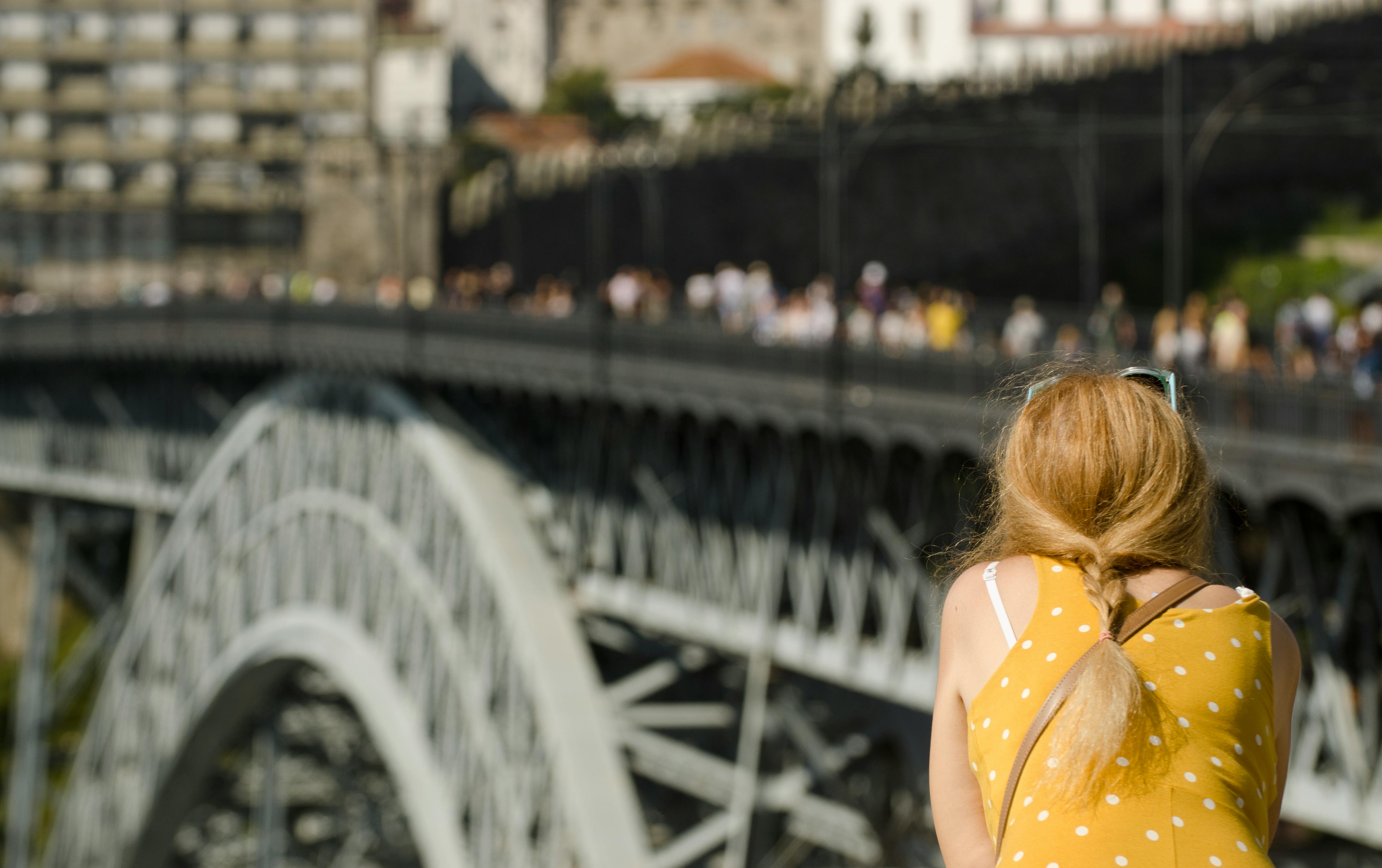 Back view of a woman in yellow dress observing a cityscape and iconic iron bridge.