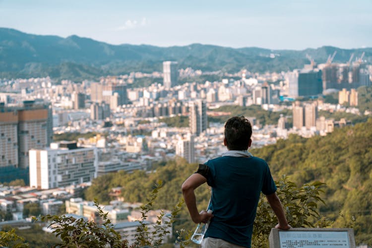 Man Holding Water Bottle Standing On Hill Overlooking City