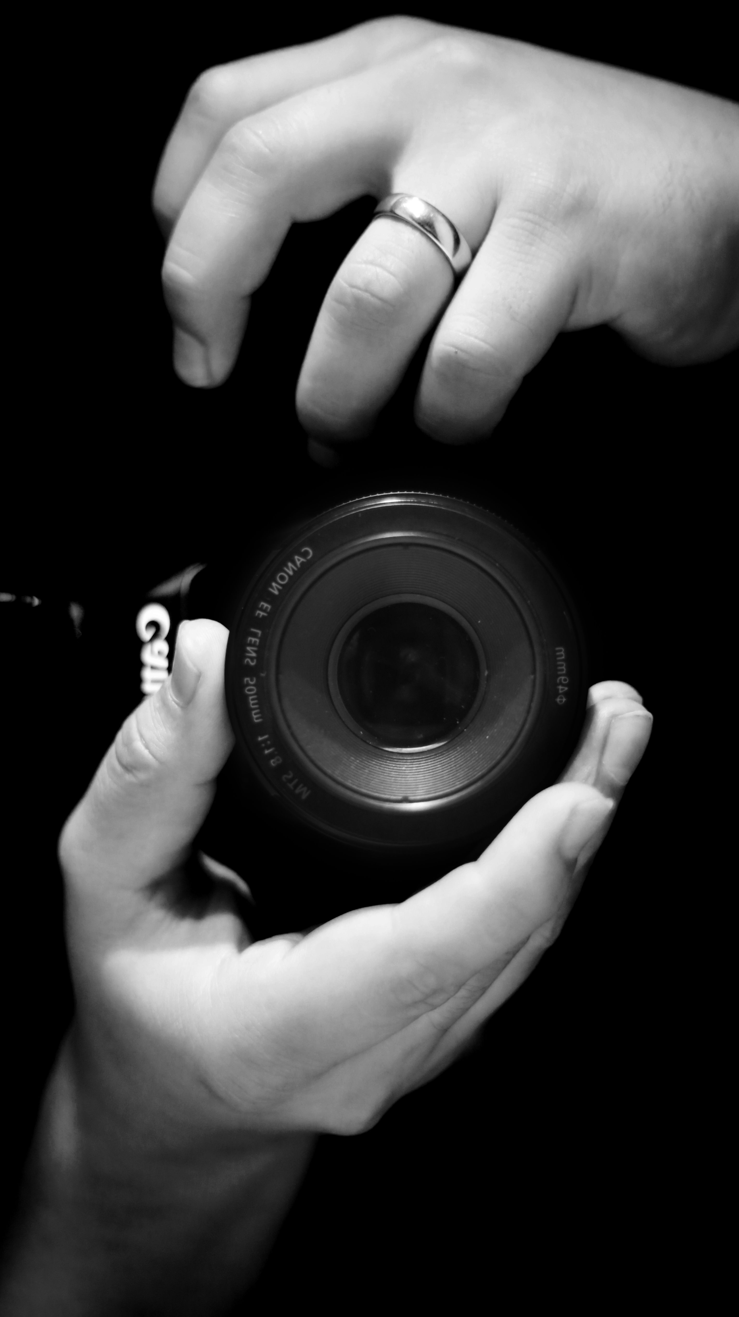 Black and white image of hands holding a DSLR camera lens, emphasizing photography tools.