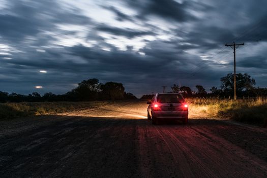 A car drives on a dirt road under a dramatic night sky in rural Argentina.