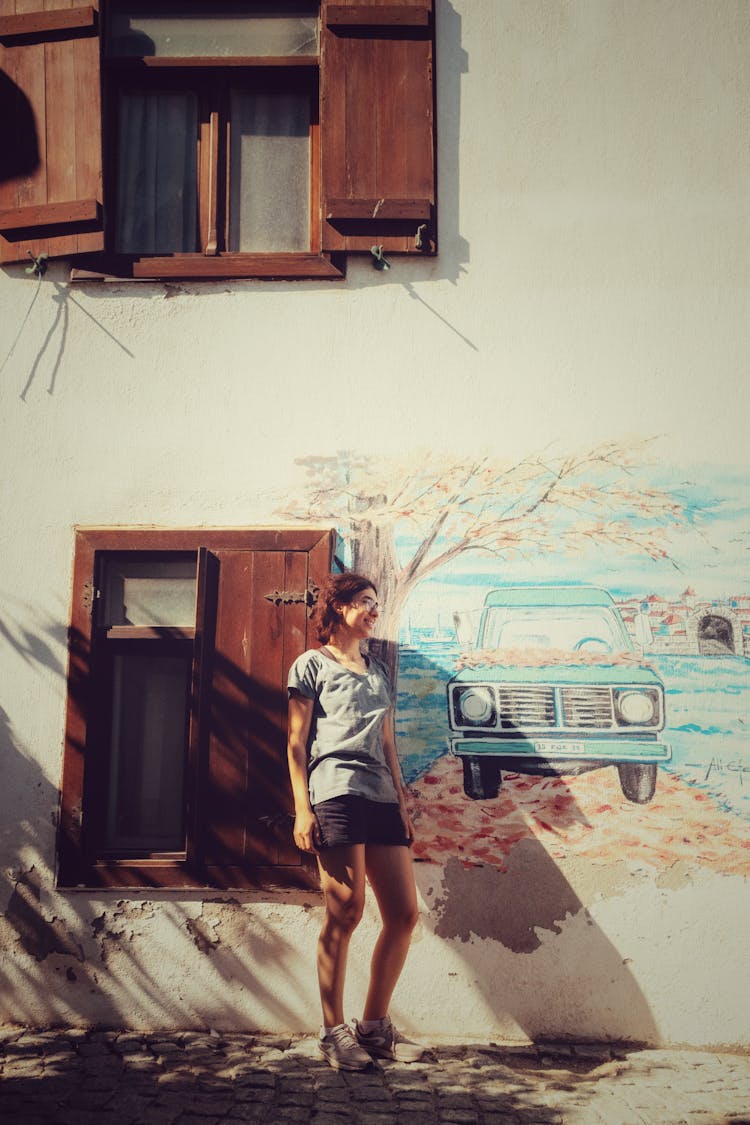 Smiling Woman Posing Next To A Picture Of A Car On A Building Wall