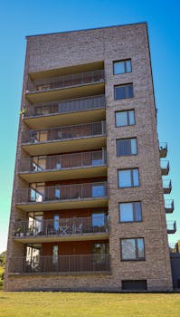Vertical shot of a modern brick apartment building with multiple balconies and clear blue sky.