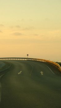A serene image of a curved road at sunrise, featuring a clear sky and gentle morning light. — photo by Furkan D