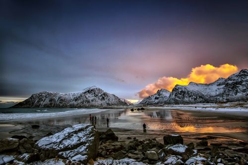 Free A breathtaking winter sunset scene with snow-covered mountains and a serene beach reflecting vibrant colors. Stock Photo