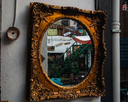 Free A decorative vintage mirror reflecting a vibrant outdoor setting with stairs and signs. Stock Photo