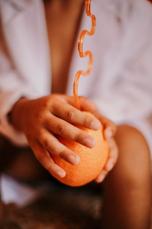 Free A Person Holding an Orange with Straw Stock Photo