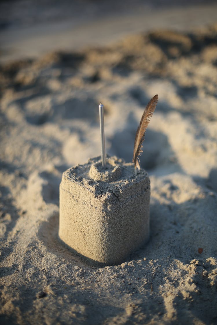 Feather And Candle On A Sand Castle