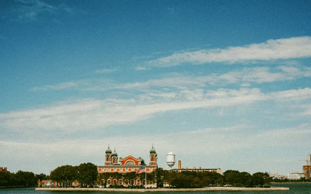 Photo: Lalada . on Pexels Scenic view of Ellis Island as the American flag waves, set against a clear blue sky.