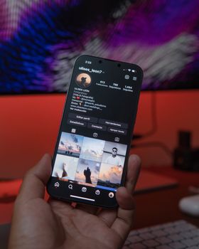 Close-up of a smartphone displaying a social media profile in a warm indoor setting.
