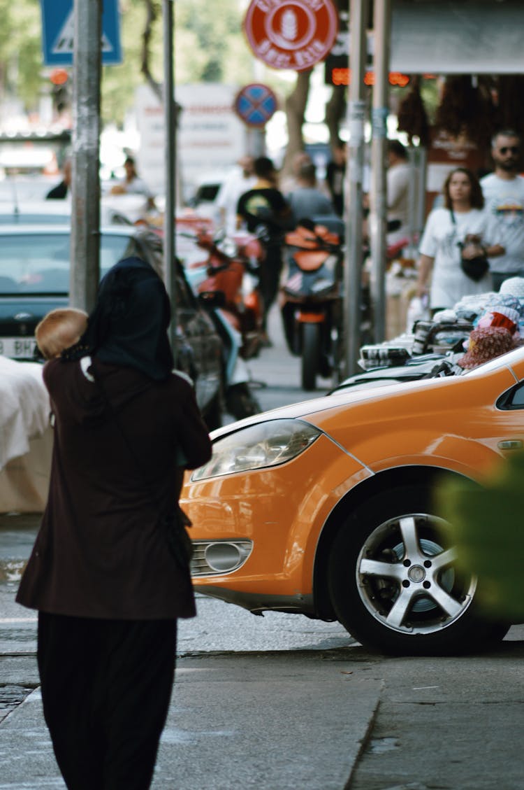 Busy People Walking On The Street Near An Orange Car 