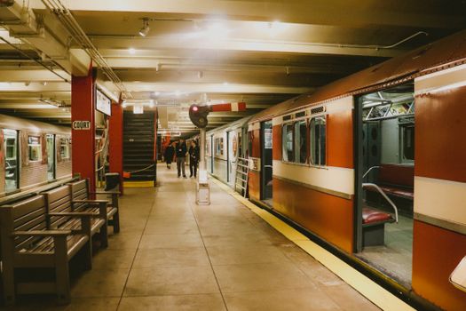 A vintage subway station platform with waiting commuters and trains, illuminated by overhead lights.