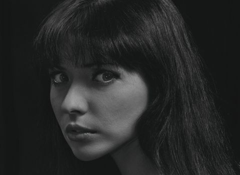Close-up black and white portrait of a young woman with a mysterious gaze.