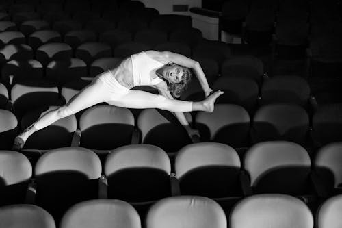 Grayscale Photo of a Woman Stretching While in a Cinema