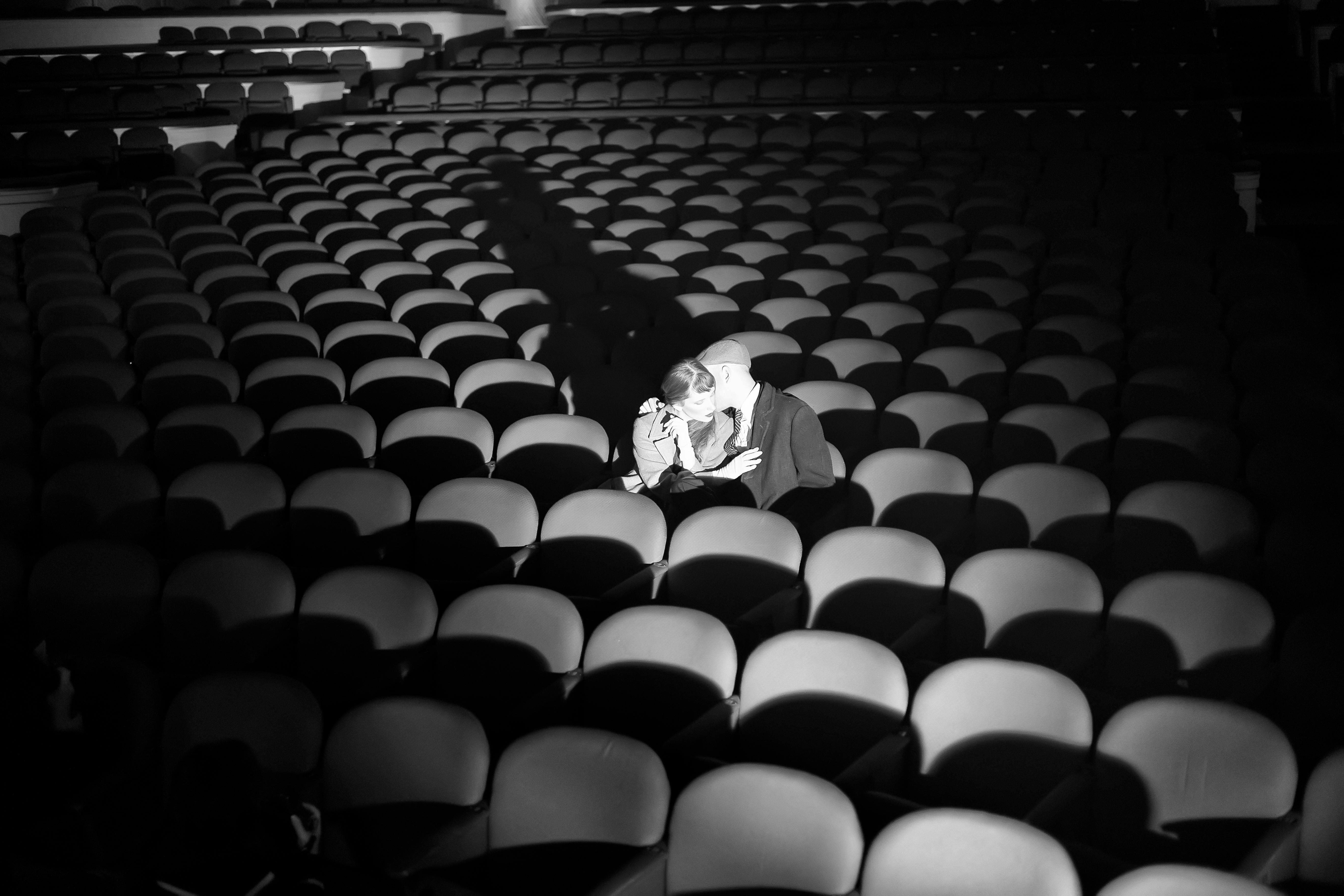 Free Black and white photo of a couple sharing an intimate moment in an empty theater. Stock Photo