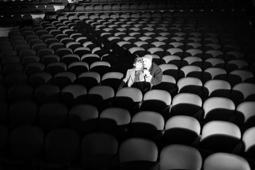 Free Couple sitting together in an empty theatre, bathed in spotlight, illustrating solitude and togetherness. Stock Photo