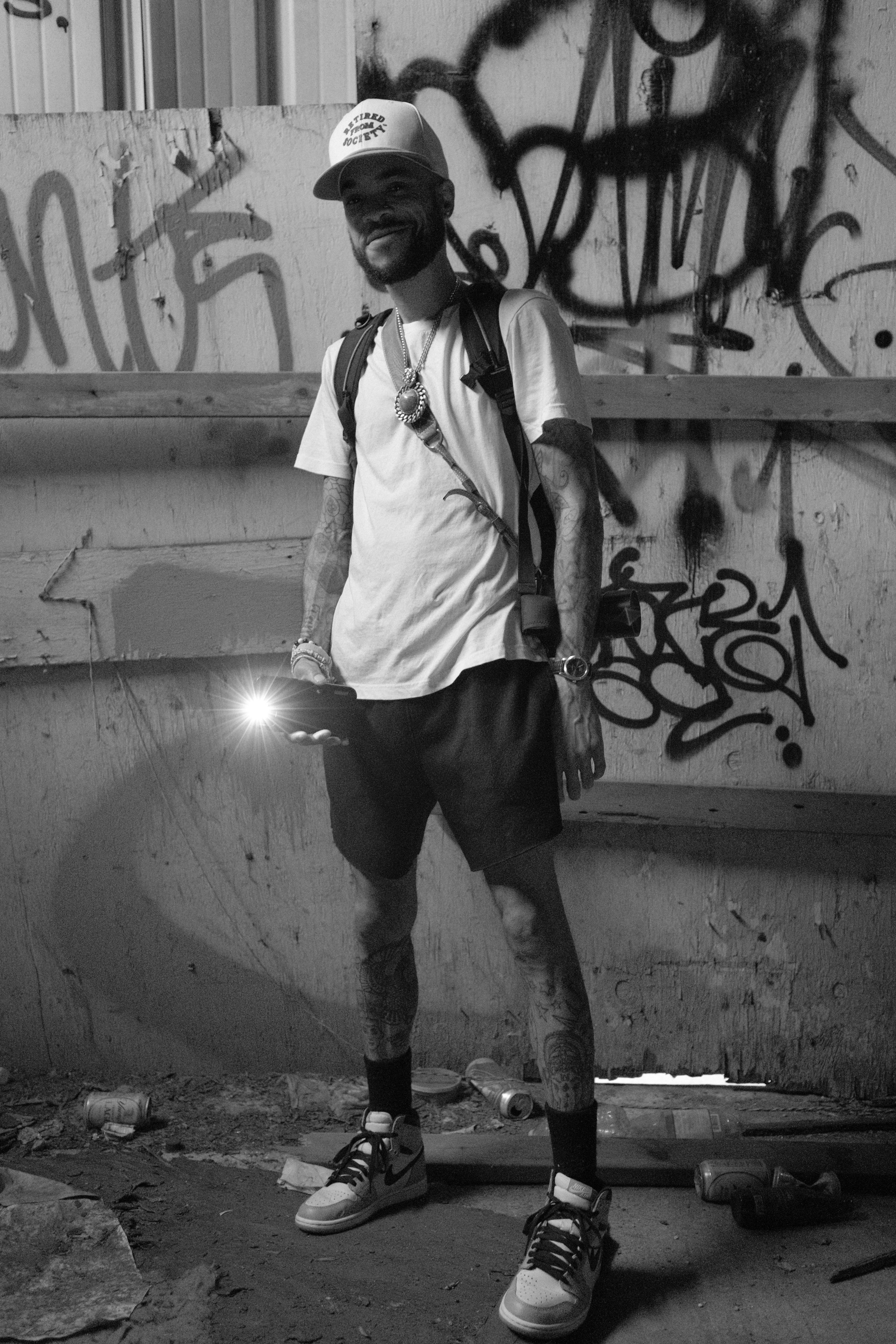 Stylish man in monochrome, showcasing urban fashion in graffiti-decorated alleyway.