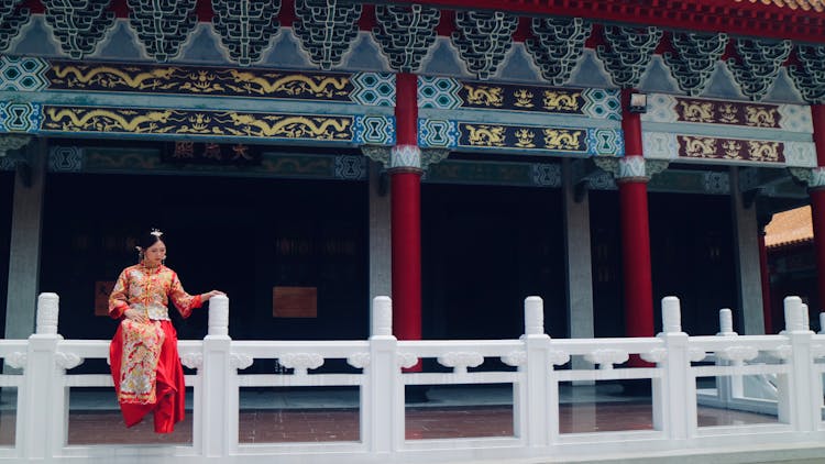 Woman In Traditional Chinese Dress Sitting On Temple Fence