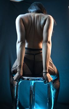 Artistic backview of a woman in a mesh outfit seated on a stool, highlighting form and texture.