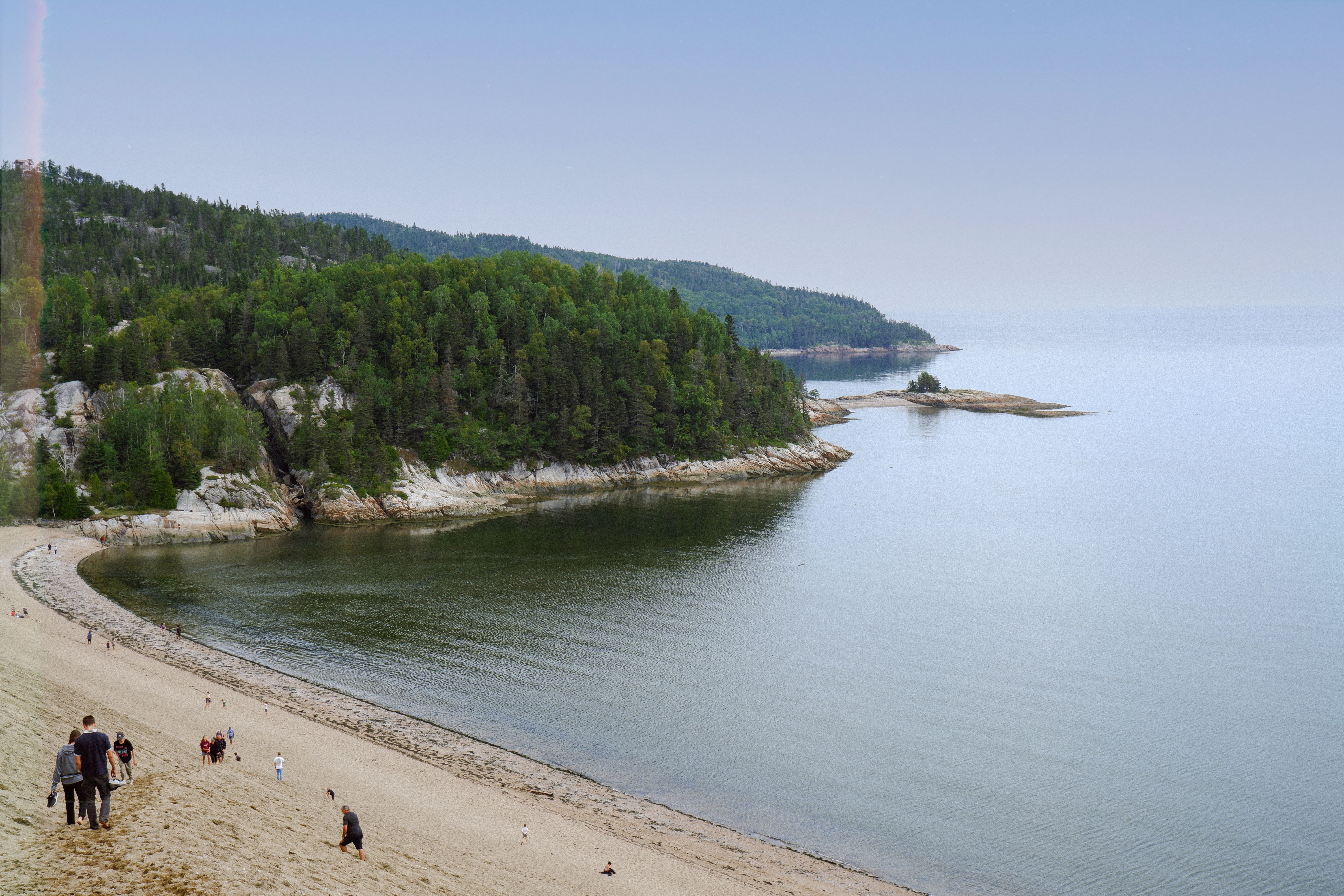 A serene beach scene with people walking along the shore and lush greenery in the background.
