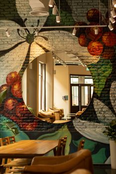 Vibrant wall art with a circular mirror reflecting cozy chairs and tables in a stylish interior setting.