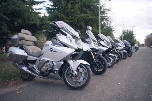 Free A row of parked motorcycles lined up on a tree-lined roadside during the day. Stock Photo