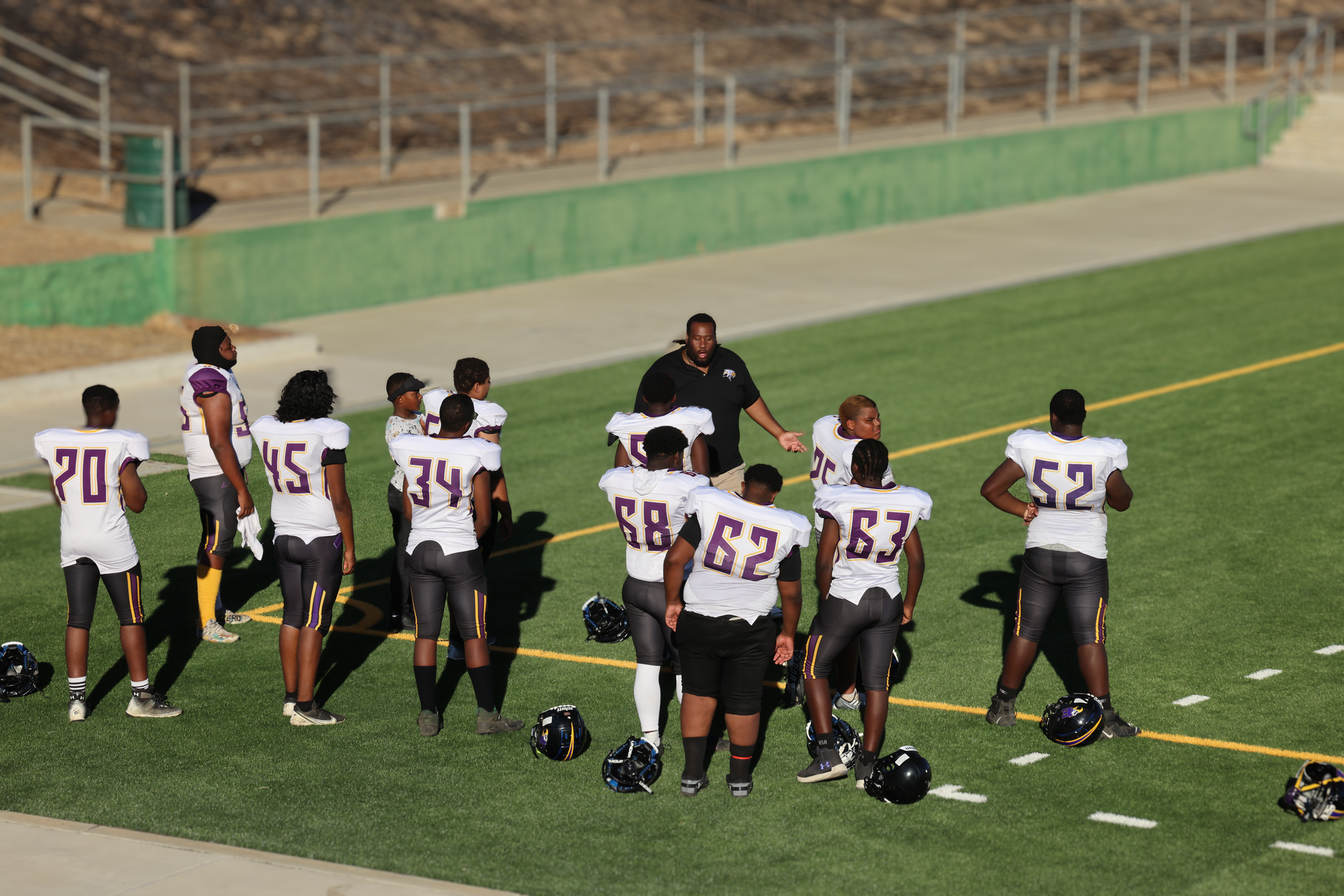 High school football team preparing on the field with coach guidance.