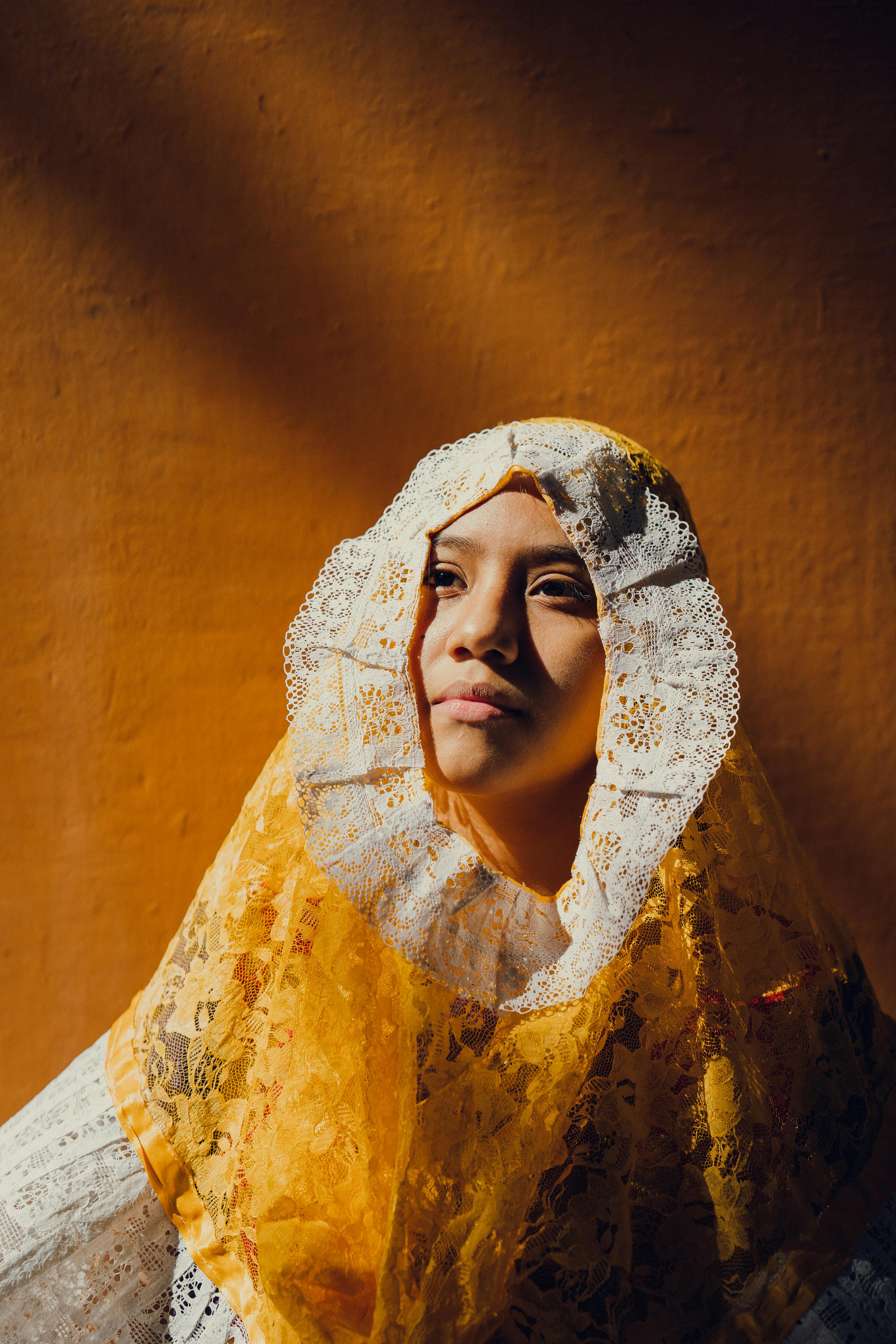 A woman in traditional Mexican attire with a lace headscarf against a warm-toned background.