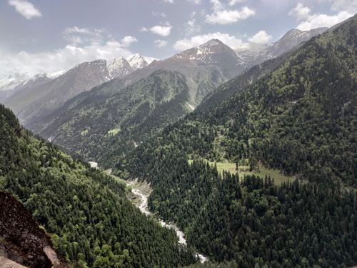 Free A breathtaking aerial shot showcasing lush forest valleys and snow-capped mountains under a bright sky. Stock Photo