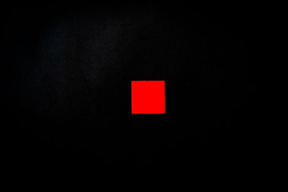 Vivid red square centered on a minimalist black background, creating a striking visual contrast.