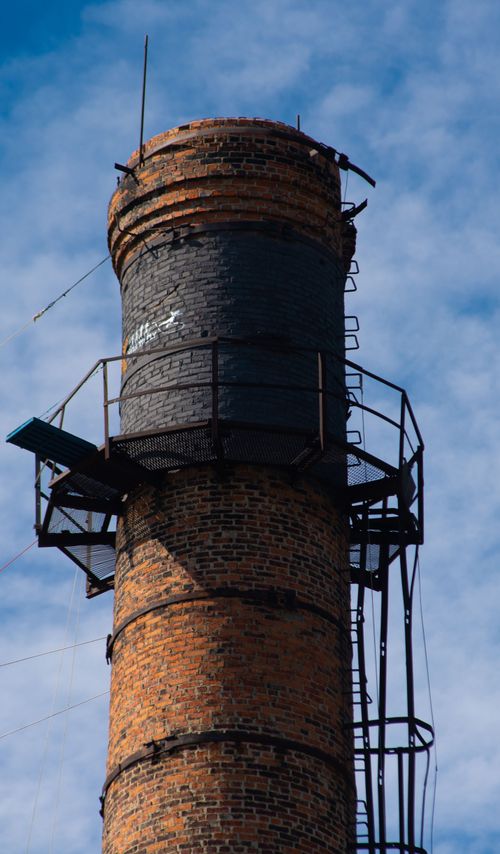 Free Close-up of an industrial brick chimney with metal structures on a clear, blue sky background. Stock Photo