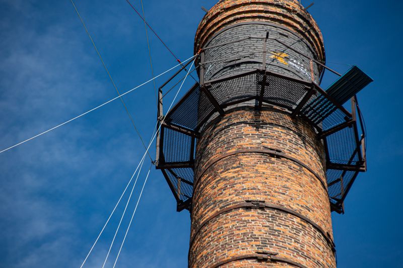 Low angle view of an old brick chimney with supportive structures against a clear blue sky.