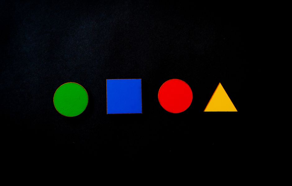 Colorful geometric shapes contrasting against a dark background, featuring circle, square, triangle.