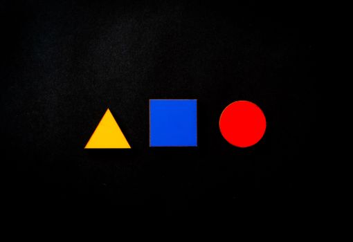 Vivid geometric shapes of triangle, square, and circle in primary colors on a black background. — photo by Magda Ehlers