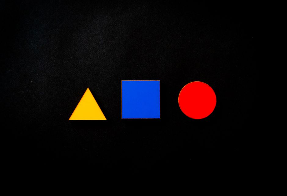 Vivid geometric shapes of triangle, square, and circle in primary colors on a black background.