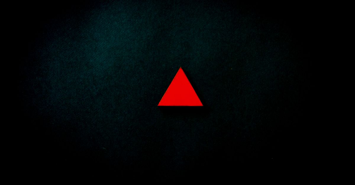 A striking minimalist image of a red triangle centered on a dark, textured background.
