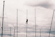 一个大胆的人在阴沉的天空下爬上帆船桅杆，展示了冒险和技巧