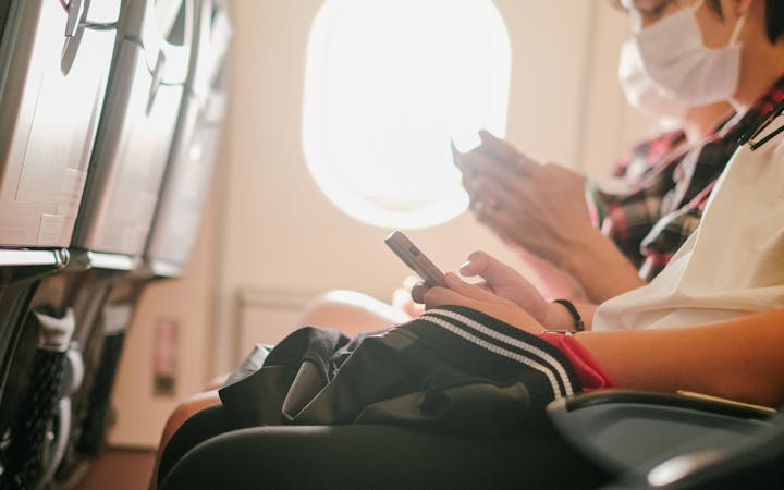 Passengers wearing masks using smartphones during flight onboard an airplane.