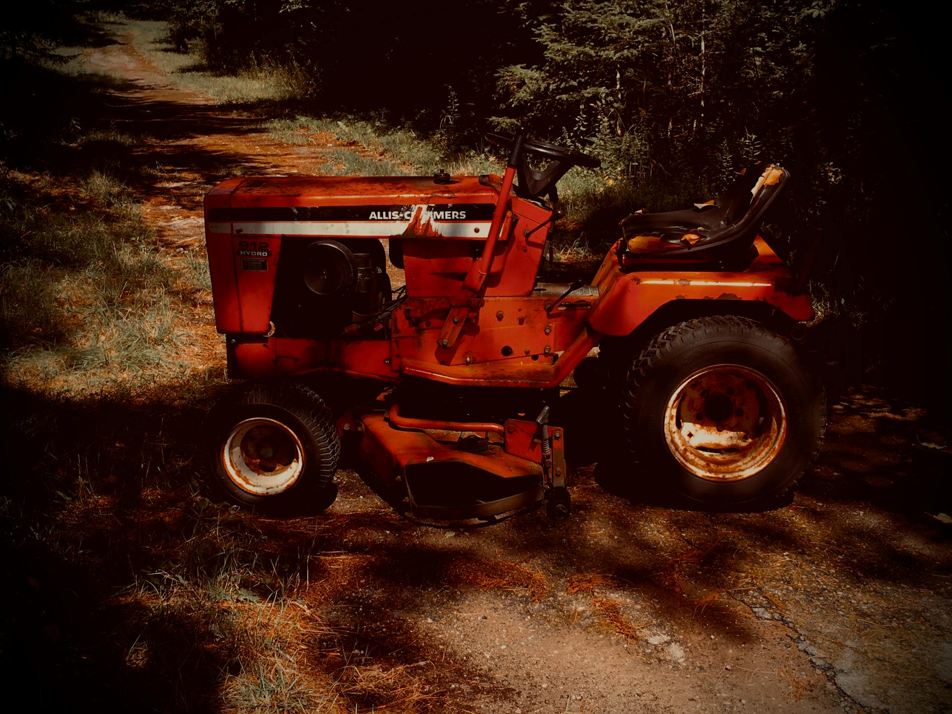 A classic red lawn tractor parked on a scenic dirt road surrounded by nature.