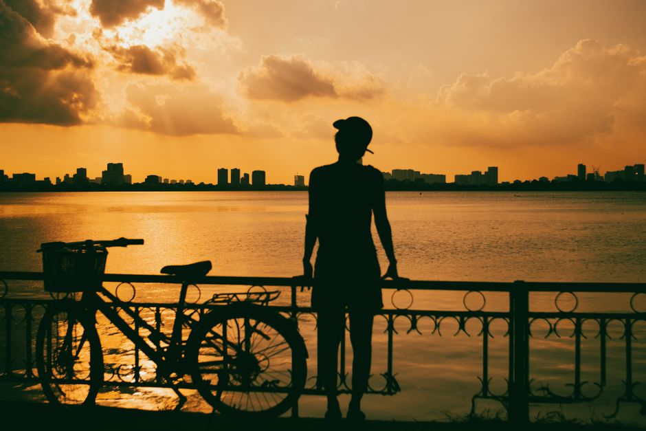 Silhouette of a man and bicycle against a vibrant sunset skyline over a river in Vietnam.