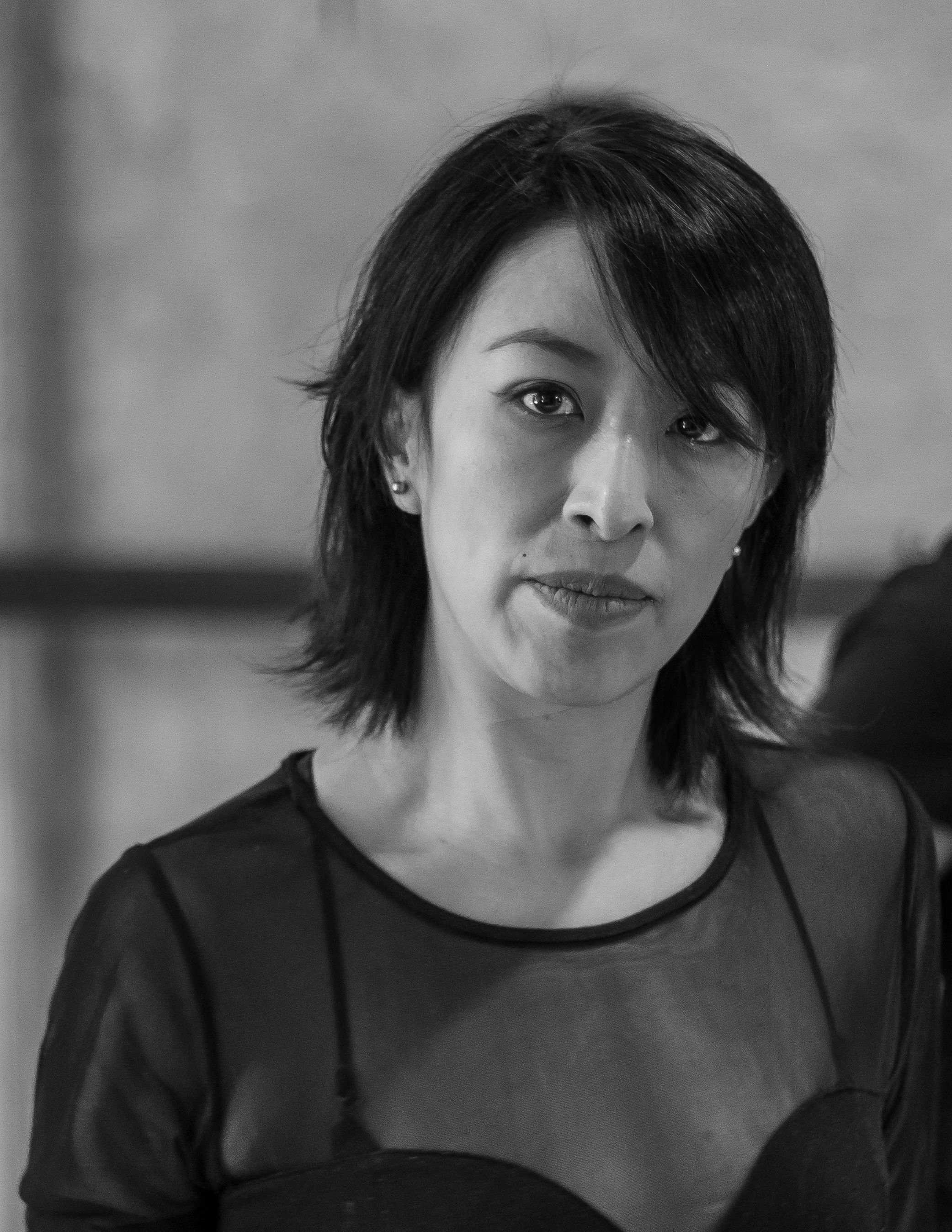 Grayscale portrait of a serious Asian woman with short hair, indoor setting.