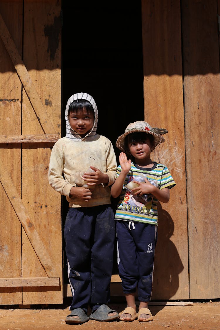 Children Standing And Waving Near A Wooden Door