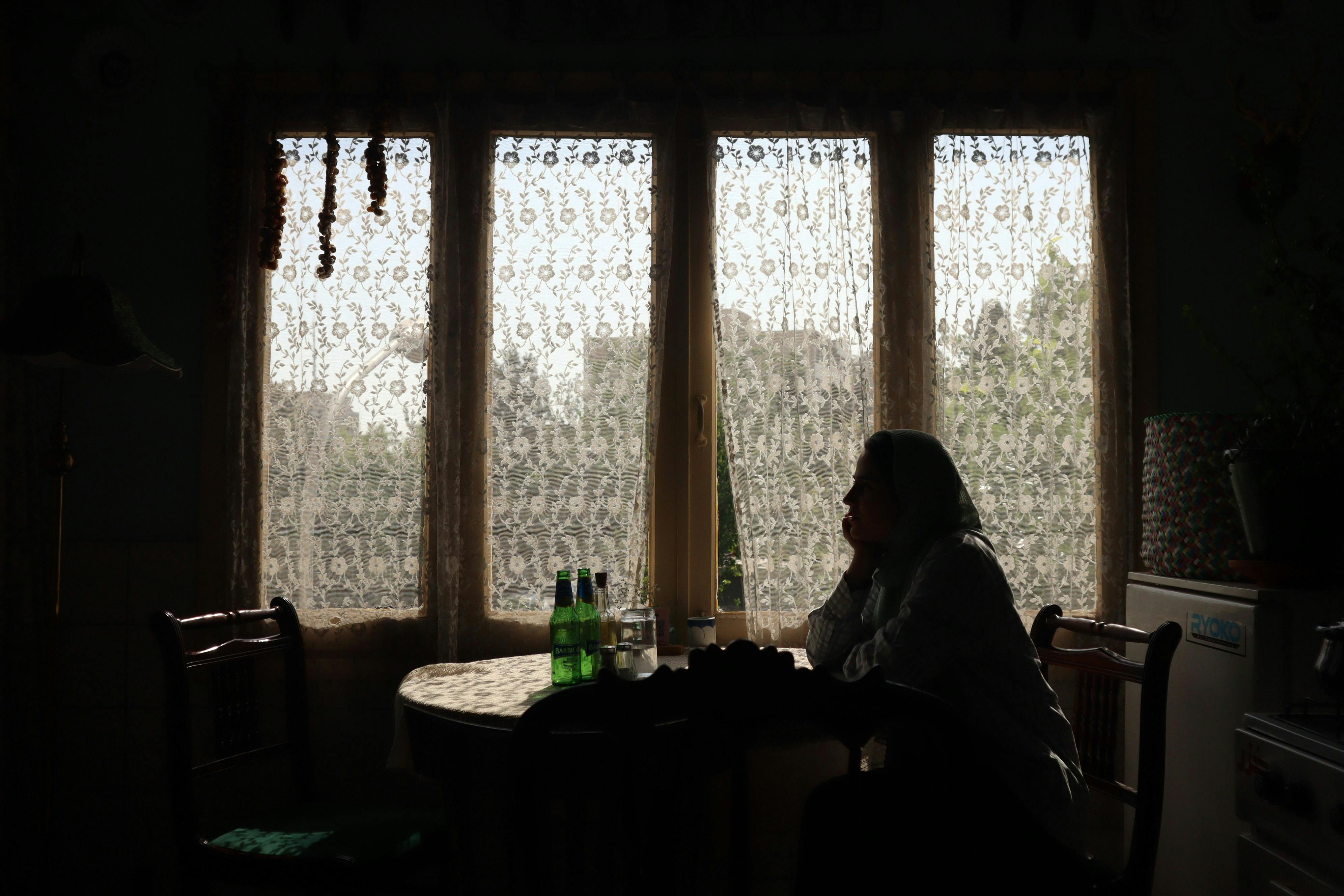 Silhouette of person sitting by a window, lost in thought in a cozy Ujjain home.