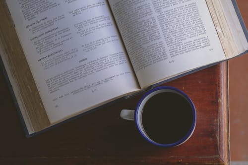 An Open Book Beside a Cup of Coffee on a Wooden Surface