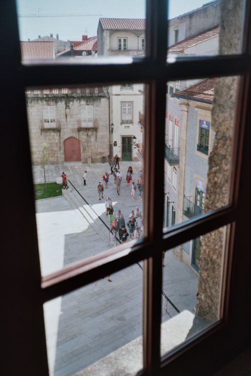 Free A charming view through a window showcasing a small town square with people walking. Stock Photo