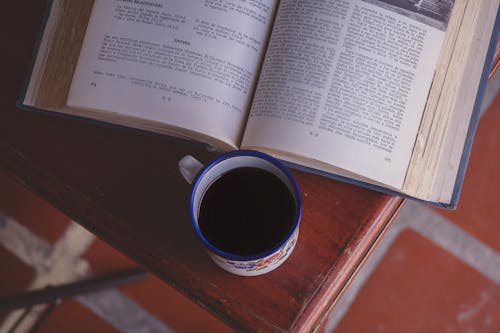 A Mug of Black Coffee Beside an Open Book on a Wooden Surface