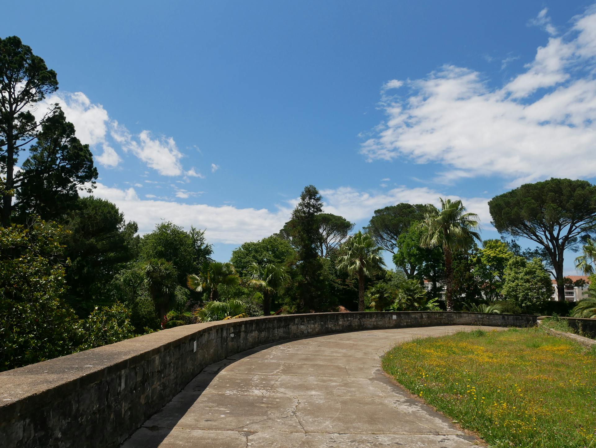 Scenic outdoor walkway surrounded by lush greenery under a clear blue sky in Bayonne, France.