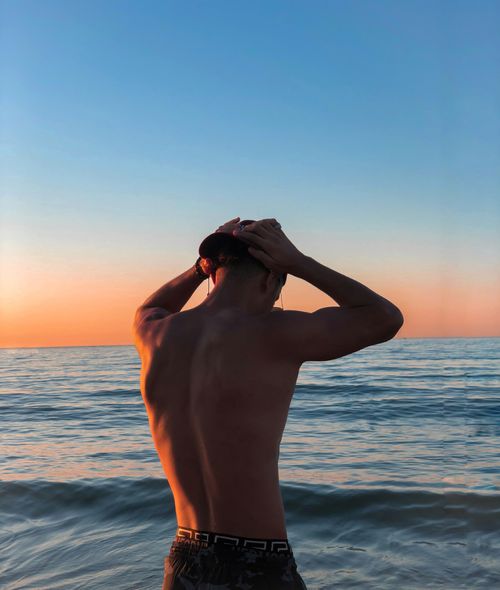 Free A young man stands by the ocean, gazing at the sunset sky. Stock Photo