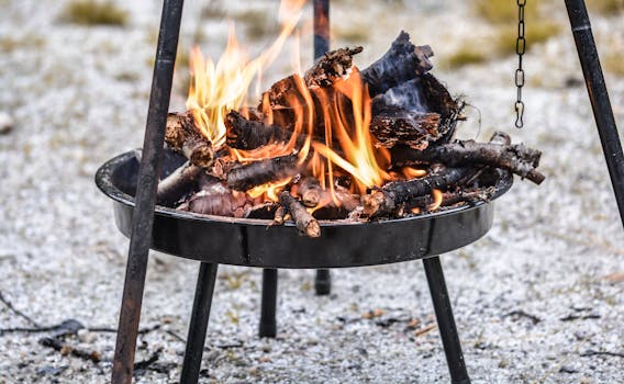 A vibrant outdoor campfire with burning wood on a tripod grill.