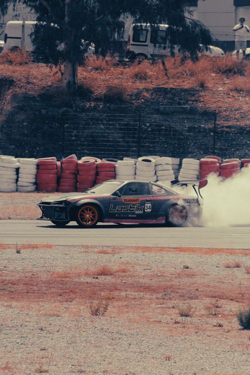 Free A car skillfully drifts around a race track corner amidst colorful barriers. Stock Photo
