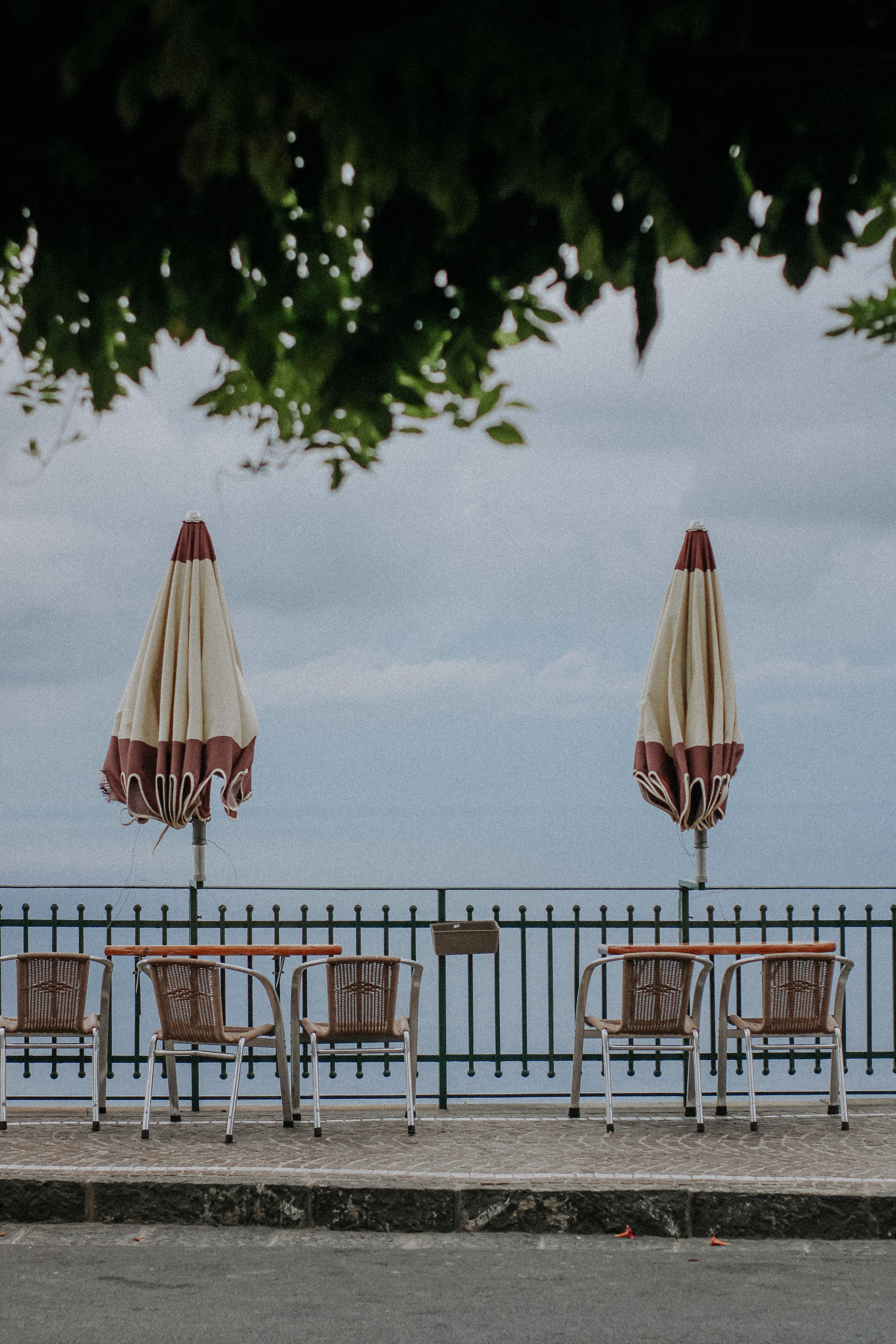 Empty chairs and closed umbrellas at a seaside cafe with ocean view.
